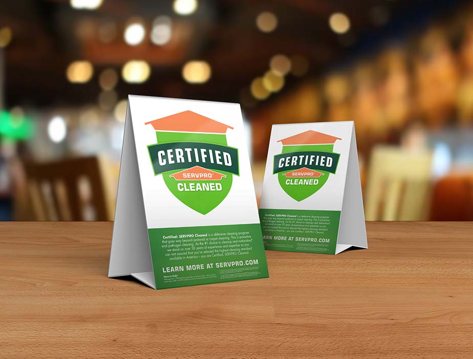 Table tent signs describing the Certified: SERVPRO Cleaned program on top of a wooden table.